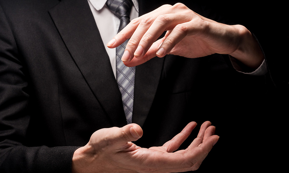 Close up of man in black suit with hand gesture on black backgro